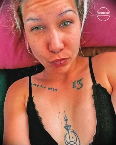 Фото тату надписи 'love her wild' и символа на груди девушки. Эскиз татуировки выполнен в минималистичном стиле черными чернилами.