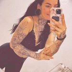 Фотография девушки, демонстрирующей детализированные татуировки на руках и плечах. Подчеркивает красоту и сложность татуировок в различных стилях.