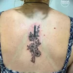 Фото татуировки на спине с изображением кинжала, обвитого розами. Детализированный рисунок, черный цвет, женственная композиция.