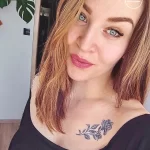 Фотография девушки с татуировкой в виде небольшой веточки с листьями на ключице. Рисунок выполнен в черных тонах.