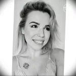 Фотография девушки с татуировкой в виде небольшого цветка на ключице. Рисунок выполнен в черных тонах.