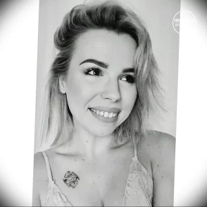 Фотография девушки с татуировкой в виде небольшого цветка на ключице. Рисунок выполнен в черных тонах.