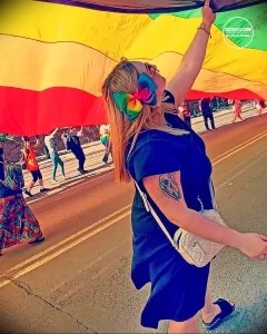 Фото тату на плече девушки, держащей радужный флаг. Виден фрагмент татуировки с изображением птицы.