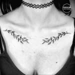 Фотография женщины с татуировкой в виде двух ветвей, расположенных симметрично на груди. Татуировка выполнена в тонком, минималистичном стиле.