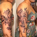 Фотография женского плеча, украшенного большой татуировкой с изображением различных цветов, выполненной в технике blackwork.