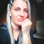 Фото тату на руках девушки: изображение кошки и абстрактные линии, выполненные в черном цвете. Девушка смотрит в камеру и улыбается.