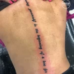 Фото татуировки с надписью "Loving yourself is the beginning of a love for life" на боку девушки. Минималистичный дизайн и вдохновляющий текст.