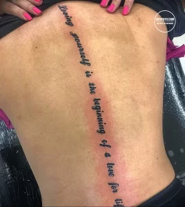 Фото татуировки с надписью "Loving yourself is the beginning of a love for life" на боку девушки. Минималистичный дизайн и вдохновляющий текст.
