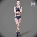 Фото девушки с полностью покрытым татуировками телом. Разнообразные рисунки, яркие цвета. Девушка стоит в позе уверенности.