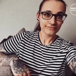 Фото девушки в полосатой футболке с множеством татуировок на руках, демонстрирующих разнообразие стилей и сюжетов.