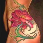 Фото тату: цветная татуировка с изображением цветка лотоса на боку. Эскиз выполнен в реалистичном стиле с использованием ярких оттенков розового и зеленого.
