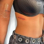 Фото тату надписи «Que sera, sera» на боку девушки. Минималистичный шрифт, тонкие линии, нежная кожа. Идеально для любителей лаконичных рисунков.