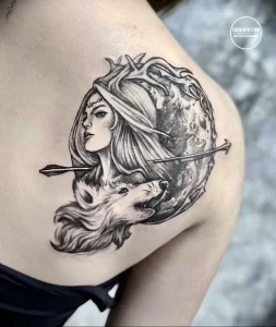 Фото татуировки на спине девушки с изображением волка, смотрящего на луну. Татуировка выполнена в черно-белых тонах, с детальной проработкой шерсти и лунного света.