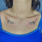 Фото тату на груди: две симметричные веточки с листьями. Минималистичный рисунок татуировки, выполненный в черном цвете.