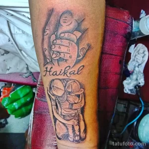 Фото тату на предплечье с изображением мультяшного персонажа и надписью "Haikal". Рисунок татуировки выполнен в черно-белых тонах с использованием контуров.