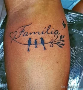Фото татуировки на руке с надписью 'Familia' и изображением трех птиц. Рисунок выполнен в минималистичном стиле черными чернилами.