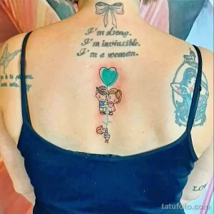 Фото татуировки на спине с надписью "I'm strong. I'm invincible. I'm a woman." и изображением воздушных шаров в форме сердца, выполненной в ярких цветах.