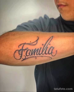 Фото татуировки на руке с надписью 'Familia' каллиграфическим шрифтом. Простой и элегантный рисунок татуировки.