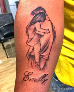 Фото тату на руке с изображением отца, обнимающего дочь. Надпись "Emily" расположена под рисунком. Черно-белый минималистичный стиль.