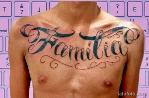 Фото тату на груди с надписью 'Familia', выполненной красивым шрифтом с элементами декора. Черно-синяя татуировка.