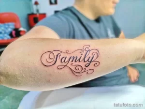 Фото тату надписи 'Family' черным цветом, выполненной каллиграфическим шрифтом на предплечье. Изящный рисунок татуировки для тех, кто ценит семью.