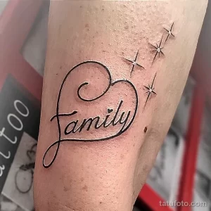 Фото тату надписи 'Family' в форме сердца, украшенной маленькими звёздами, на женском предплечье. Изящный шрифт и тонкие линии.
