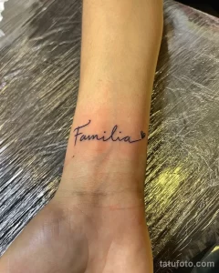 Фото тату на запястье: надпись 'Familia' выполненная изящным шрифтом с маленьким сердечком рядом. Черно-белый рисунок.