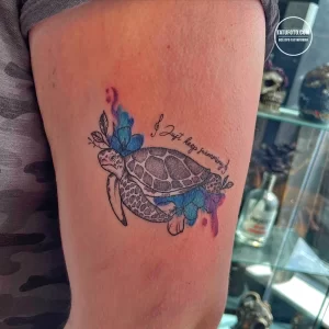 Фото тату черепахи с надписью "Just keep swimming", выполненной в черно-белых тонах с добавлением акварельных элементов. Рисунок расположен на руке.