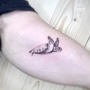 Фото минималистичной татуировки морской черепахи, выполненной в технике blackwork, на руке.