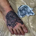 Фото тату: Черно-белая татуировка с изображением черепахи и датой '1997'. Минималистичный рисунок татуировки на стопе.