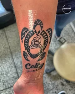 Фотография татуировки черепахи в стиле маори с надписью 'Colby' и датой на лодыжке. Черно-серая татуировка с традиционными узорами.