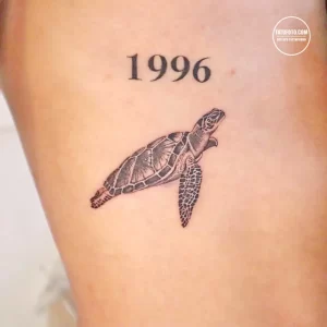 Фото татуировки черепахи с датой '1996' на руке. Простой и лаконичный дизайн, выполненный в черно-серых тонах.