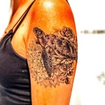 Фото тату черепахи в окружении пионов и мандалы на плече. Черно-белый рисунок, выполненный в технике дотворк.