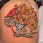 Фото тату черепахи, украшенной яркими цветами на плече. Цветной рисунок в реалистичном стиле.