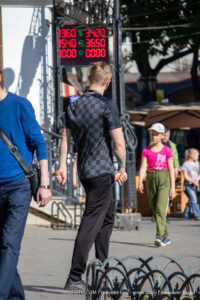 Фото тату на руке мужчины, вид сзади. Видна часть татуировки в черно-серых тонах, на фоне городская среда и рекламный щит.
