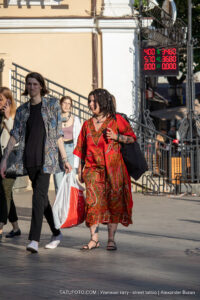 Фото тату на руке и плече девушки в ярком красном платье. Рисунок татуировки выполнен в традиционном стиле с использованием ярких цветов.