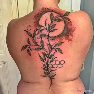 Фото тату луны с ветвями и сотами на спине девушки. Рисунок выполнен в черном цвете с добавлением акварельных пятен.