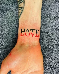 Черно-белое фото татуировки на запястье с надписью 'HATE LOVE'. Простой, минималистичный дизайн, выполненный четкими линиями.