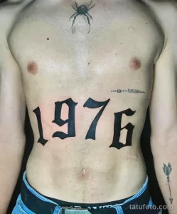 Фото татуировки на груди с большими цифрами 1976. Черный цвет, готический шрифт, минималистичный стиль.