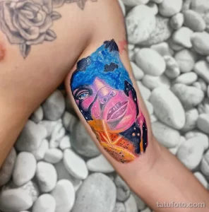 Фото тату с изображением женского портрета, выполненного в стиле акварели и с элементами космоса. Яркие цвета, плавные переходы, абстрактный дизайн. Расположена на руке.