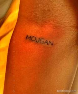 Фото тату с надписью 'MOJGAN' на руке. Минималистичный шрифт, черные чернила, аккуратное исполнение. Идеально для тех, кто ценит лаконичность.