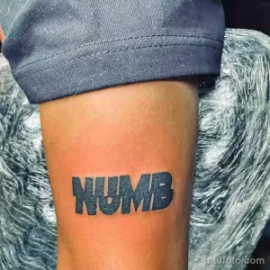Фото тату: Черная татуировка с надписью 'NUMB' выполненная крупным шрифтом на руке.