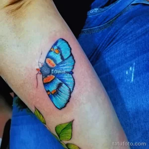 Фото тату на икре с изображением голубой бабочки. Акварельная техника, яркие цвета и изящные линии.