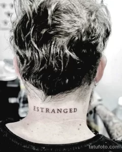 Фото тату на затылке с надписью 'ESTRANGED'. Минималистичный шрифт, черные чернила и лаконичный дизайн.