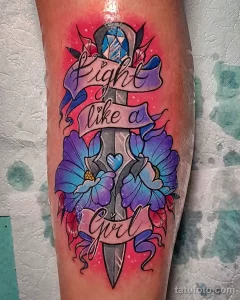 Фото тату: яркая и красочная татуировка на ноге с надписью "Fight like a girl" и изображением цветов. Мотивирующий рисунок татуировки для девушек.