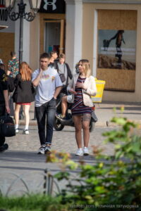 Фото тату: девушка в пиджаке и юбке, с татуировкой с портретом Джонни Деппа на бедре, держит сумку через плечо.