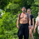 Фотография мужчины с татуировкой на груди и руке, идущего по улице. Татуировка выполнена в черно-белых тонах и имеет сложный, детализированный рисунок.