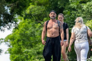 Фотография мужчины с татуировкой на груди и руке, идущего по улице. Татуировка выполнена в черно-белых тонах и имеет сложный, детализированный рисунок.