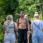 Фотография мужчины с татуировкой на груди и руке, идущего по улице. Татуировка выполнена в черно-белых тонах и имеет сложный, детализированный рисунок.