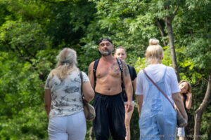 Фотография мужчины с татуировкой на груди и руке, идущего по улице. Татуировка выполнена в черно-белых тонах и имеет сложный, детализированный рисунок.